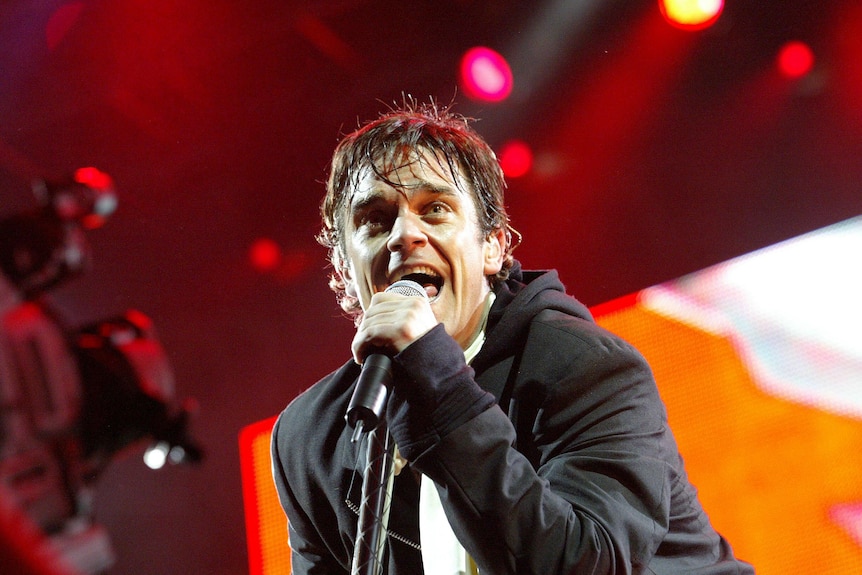 Singer Robbie Williams holds a microphone close as he sings on stage during a performance in Auckland.