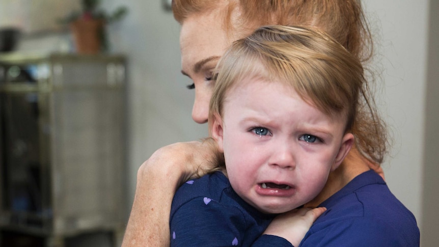 Red headed woman holding a distraught toddler over her shoulder