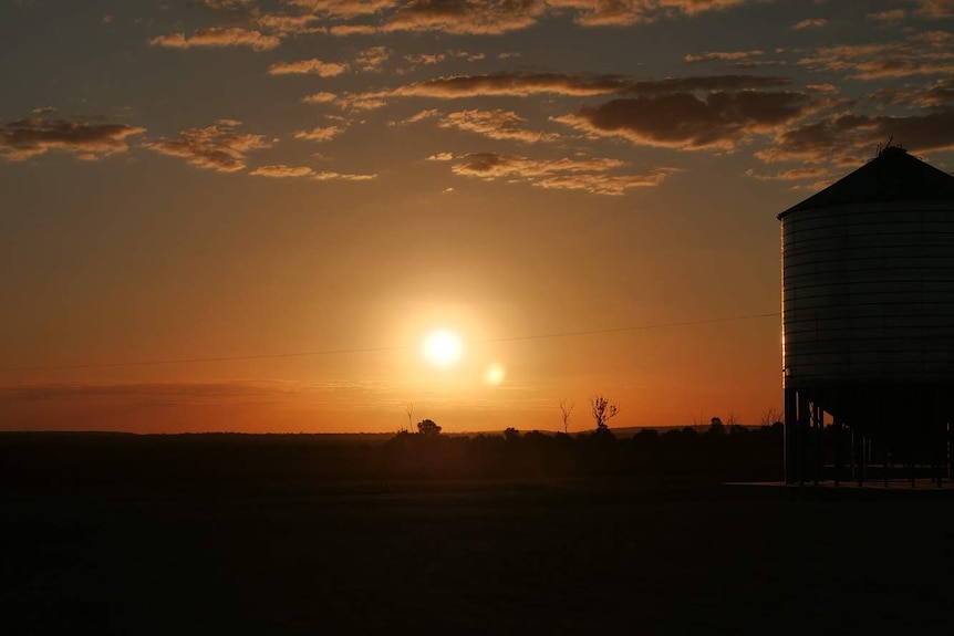 Sunset across a flat plain and reflects on grain silo