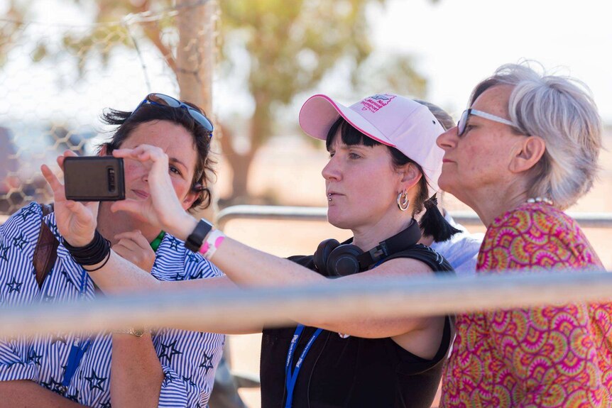 Jordin Steele holds up a phone to take a photo while two women look over her shoulder.