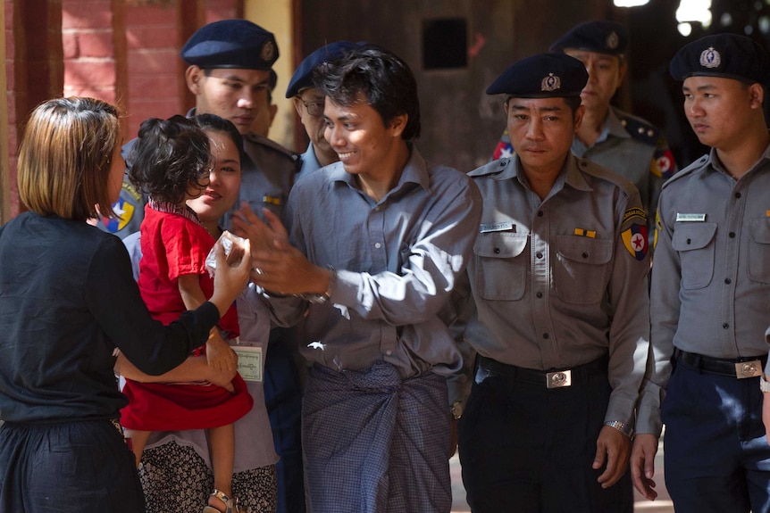 Medium shot of a man surrounded by guards greeting his family.