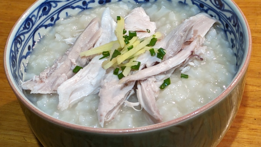 Photo of a blue and white bowl filled with white rice congee topped with chicken, ginger and spring onion