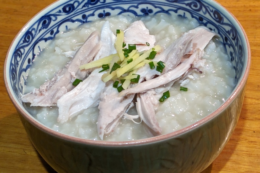 Photo of a blue and white bowl filled with white rice congee topped with chicken, ginger and spring onion