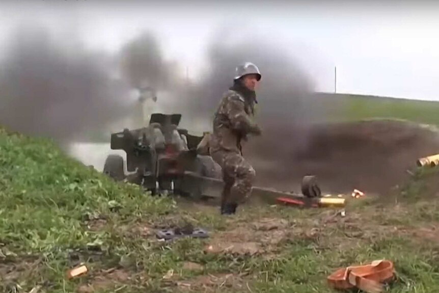 Armenian serviceman fires a cannon towards Azerbaijan as smoke rises behind them.