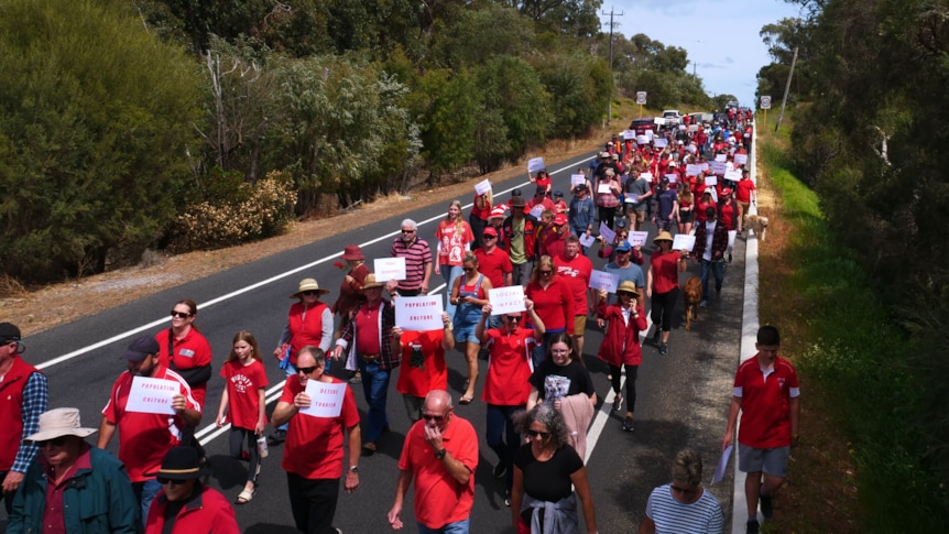 A large group of people in red shirts walk down a road