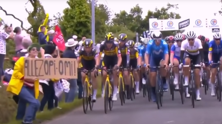 A woman holds a cardboard sign in front of a group of cyclists.