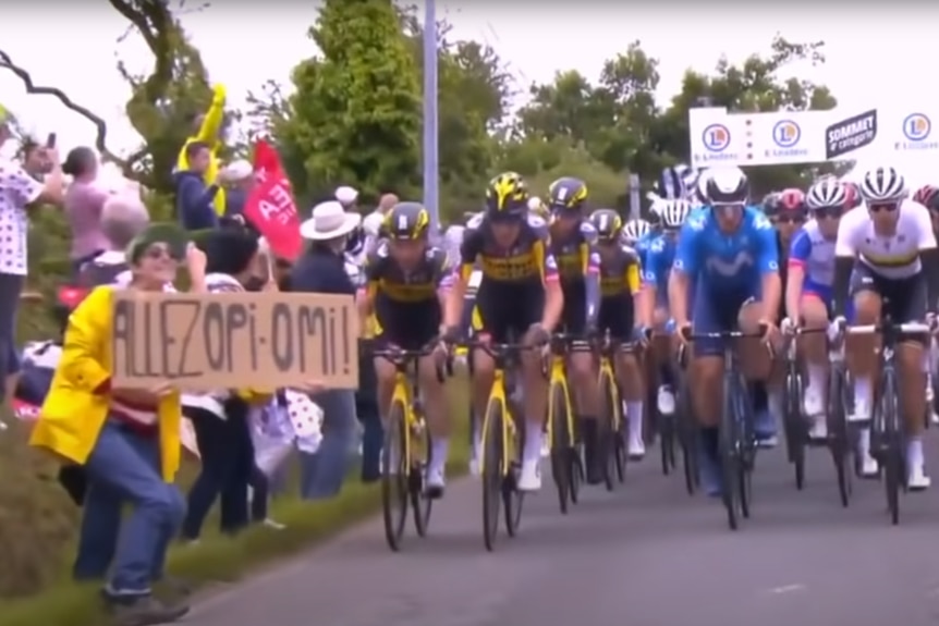 A woman holds a cardboard sign in front of a group of cyclists.