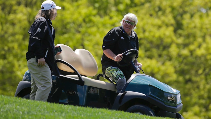 A golfer talks to a man as he gets into a golf cart on a grassy slope.