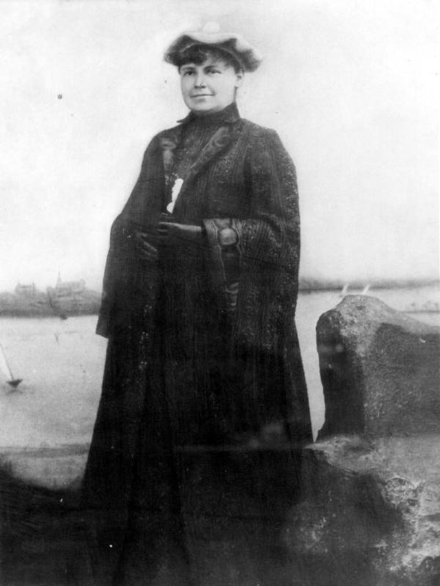 A woman wearing a bonnet and a black coat is pictured in a black and white vintage photograph.