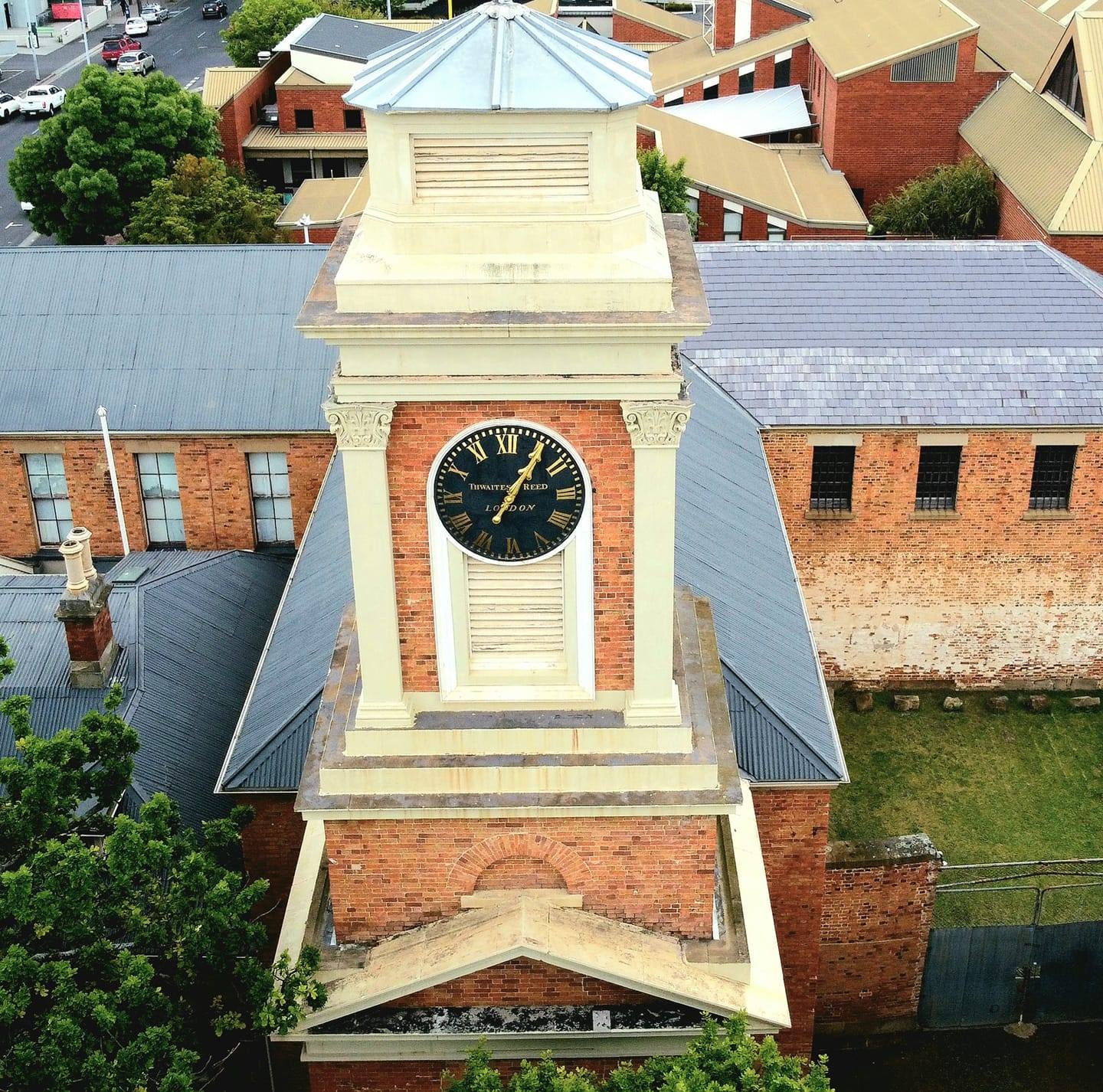 Una toma de un edificio penitenciario de ladrillo rojo con una torre de reloj y vegetación a su alrededor, tomada desde arriba.