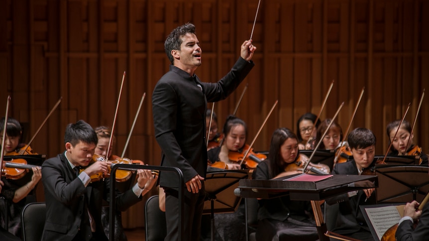 Dane Lam conducting an orchestra with his baton in the air