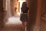 Young woman walks through ancient site wearing miniskirt and crop top.