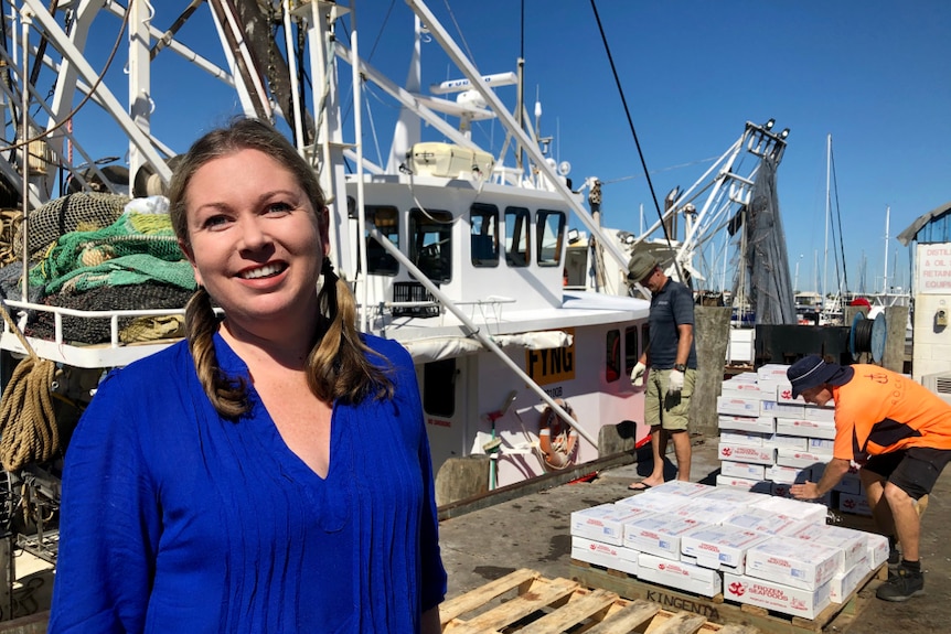 A woman stands in front of a prawn trawler unloading its catch.