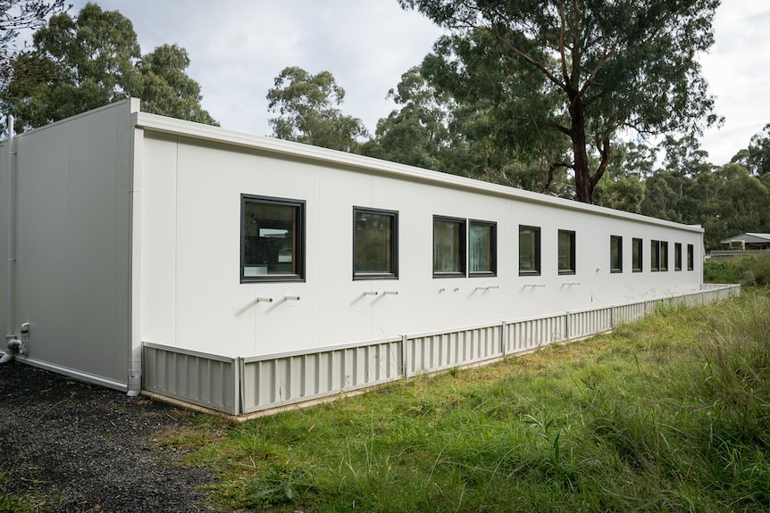 A low white building with windows sits in amongst grass.