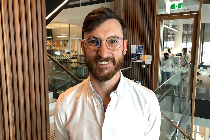 A bearded Ben is smiling and wearing an open-neck white shirt as well as tortoiseshell-rimmed glasses