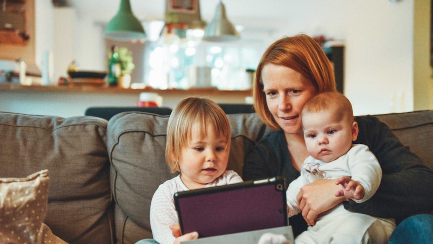 a mother and two children look at a screen while seated on a couch in a family room