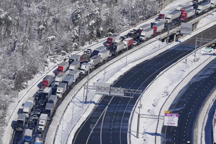 Trucks and cars line a curved stretch of highway during winter and alongside snow-covered trees