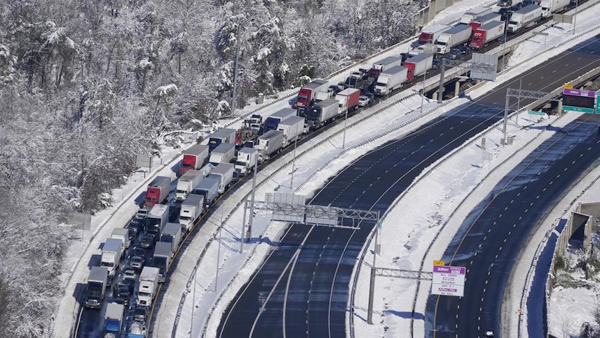 Trucks and cars line a curved stretch of highway during winter and alongside snow-covered trees