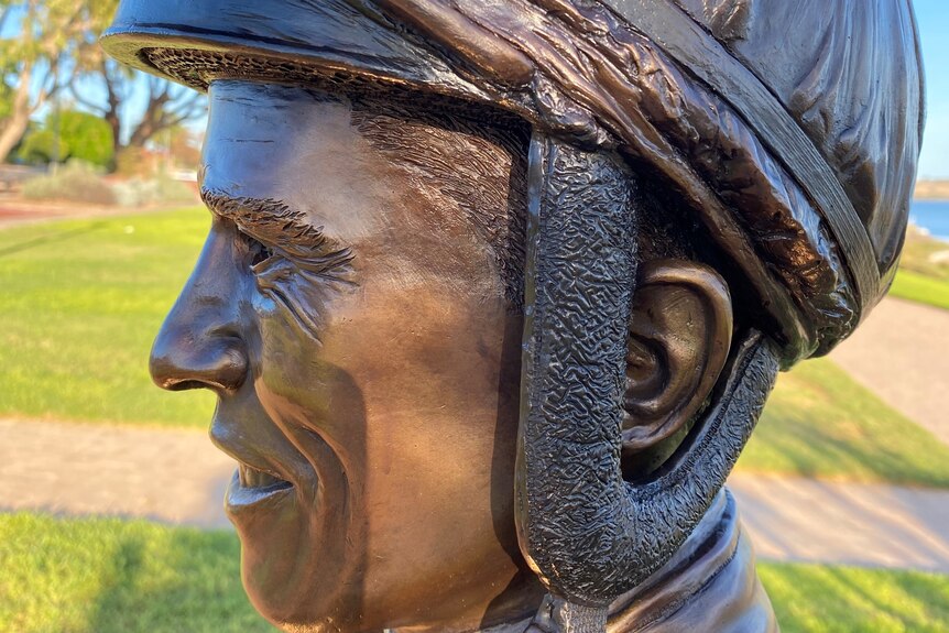 Close up of bronze jockey's head from side, with helmet with chin strap undone