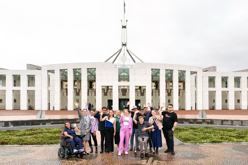 Group of 12 young people waving and smiling and standing out the front of Parliament House in Canberra