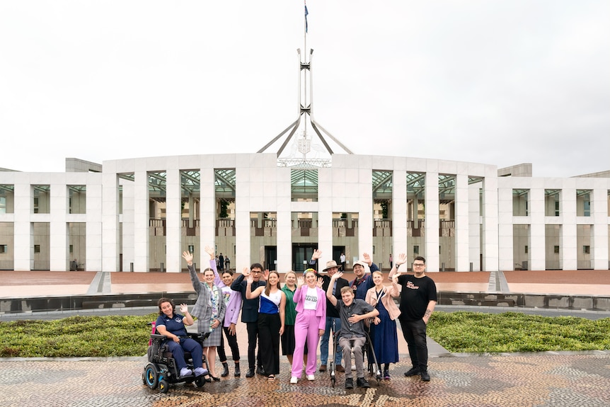 Group of 12 young people waving and smiling and standing out the front of Parliament House in Canberra