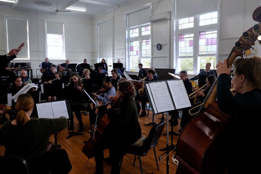 An orchestra in a big room with white walls and wood floors