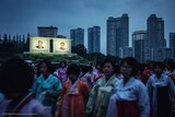 North Korean women gather in front of billboards of Kim Il-Sung and Kim Jong-Il.