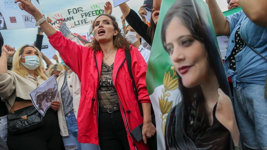 Women shout slogans during a protest while holding an image of Mahsa Amini.