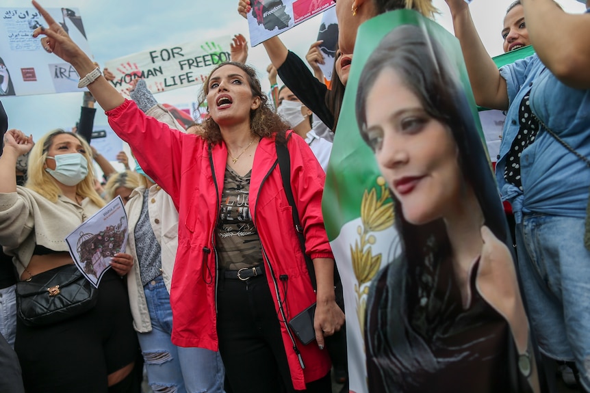 Women shout slogans during a protest while holding an image of Mahsa Amini.