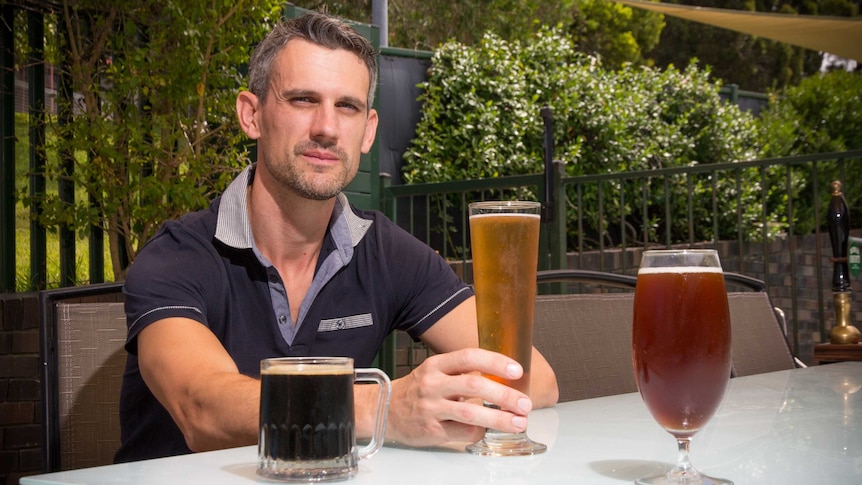 Ben Freeburn sits at a table with three beers sitting on it.