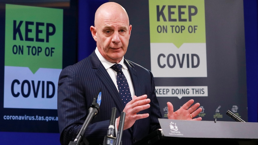 Tasmanian Premier Peter Gutwein gestures in front of a sign saying "keep on top of COVID".