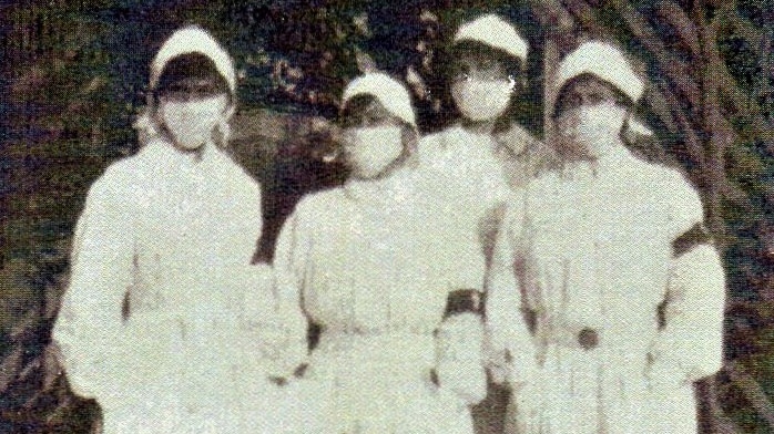 A black and white photo showing four nurses wearing masks and gowns.