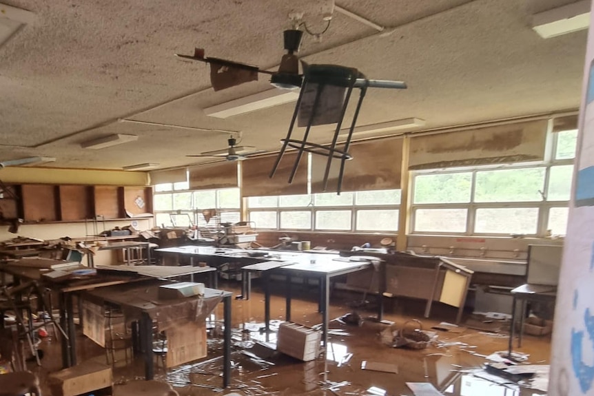 inside classroom with dirty flood water, furniture upended, including a chair hanging from the ceiling fan