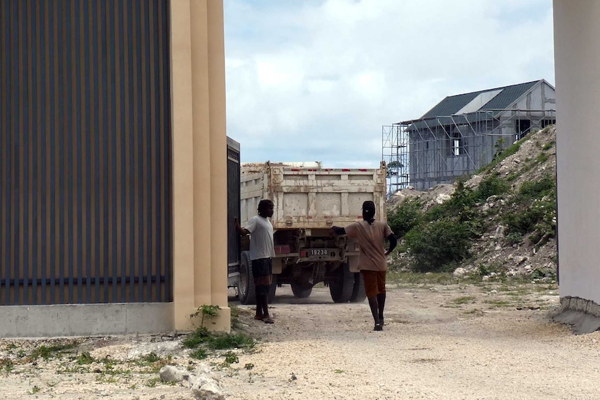 Inside the Rainbow City gates, some construction work can be seen on a structure. Two people are inside the gate, and a truck.