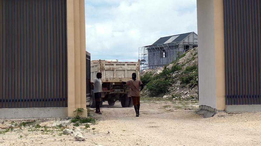 Inside the Rainbow City gates, some construction work can be seen on a structure. Two people are inside the gate, and a truck.