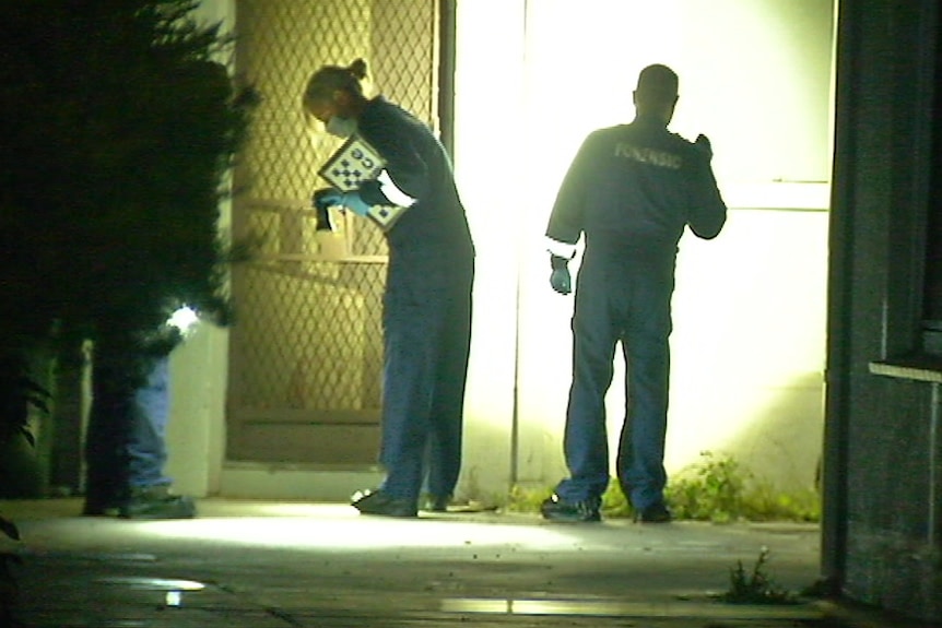 Police officers shine torches on and around a building.