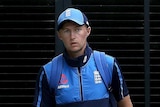 Joe Root, wearing his England tracksuit, walks past chairs at the SCG.