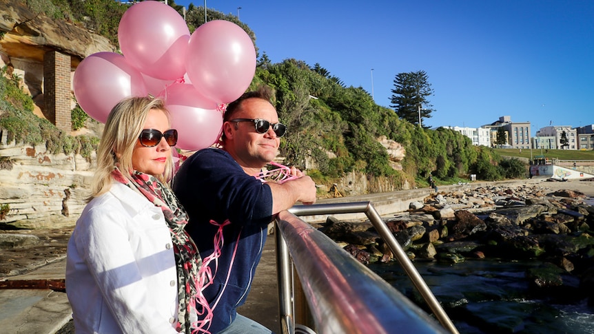 Couple standing by the beach in Sydney, holding pink balloons.