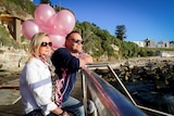 Couple standing by the beach in Sydney, holding pink balloons.