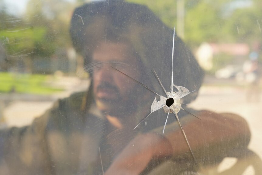 A soldier's face, out of focus, with a large bullet hold in glass in focus in the foreground