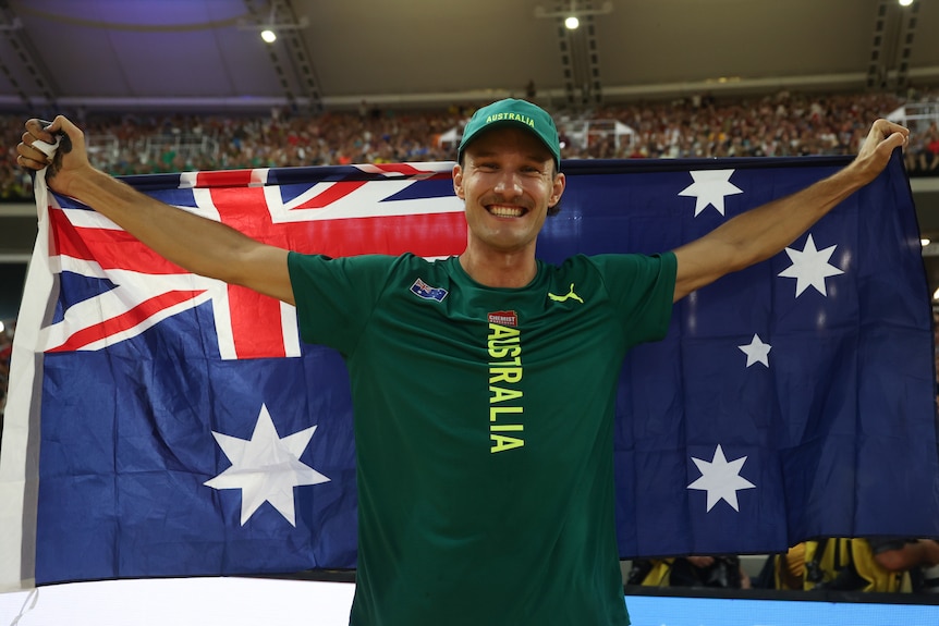 An Australian male pole vaulter stands holding the national flag behind him at the Budapest World Championships.