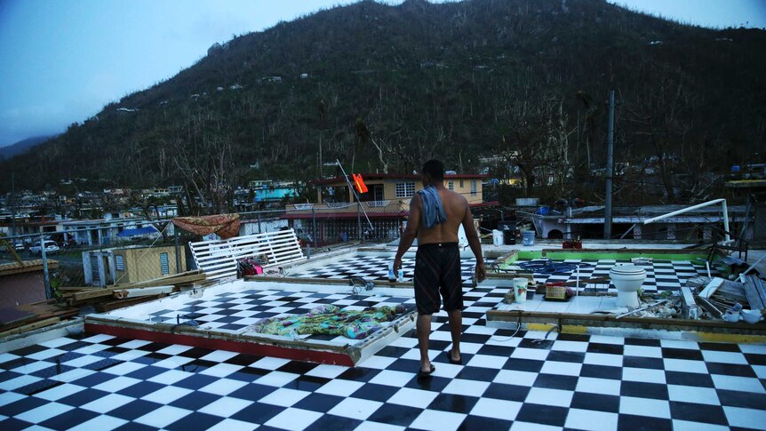 A man walks on the upstairs floor of his home, where the walls were blown off, in the aftermath of Hurricane Maria