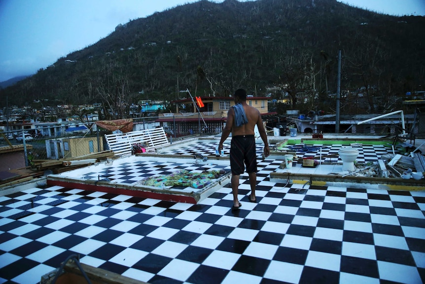 A man walks on the upstairs floor of his home, where the walls were blown off, in the aftermath of Hurricane Maria