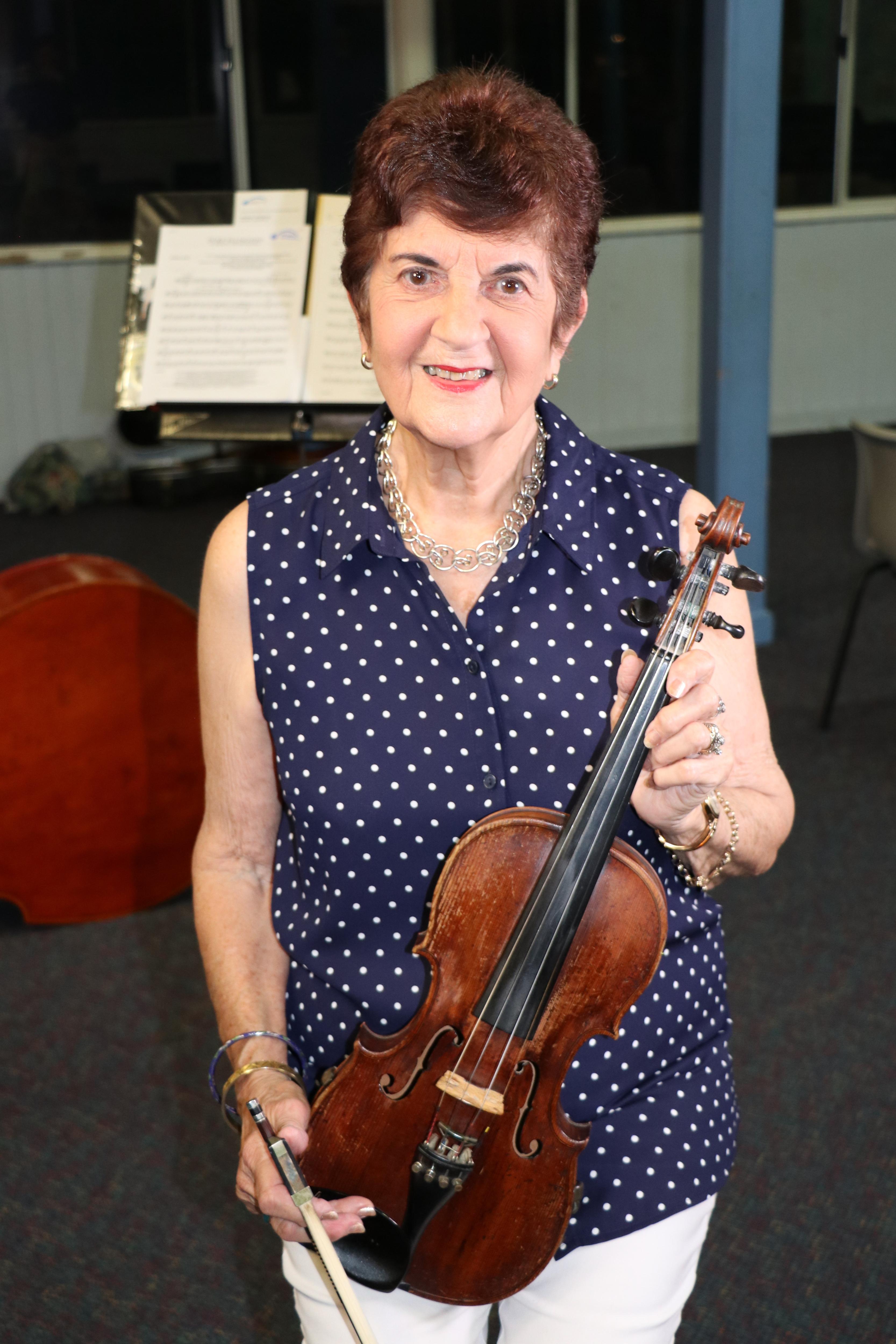 a woman smiles and holds her violin looking directly at the camera