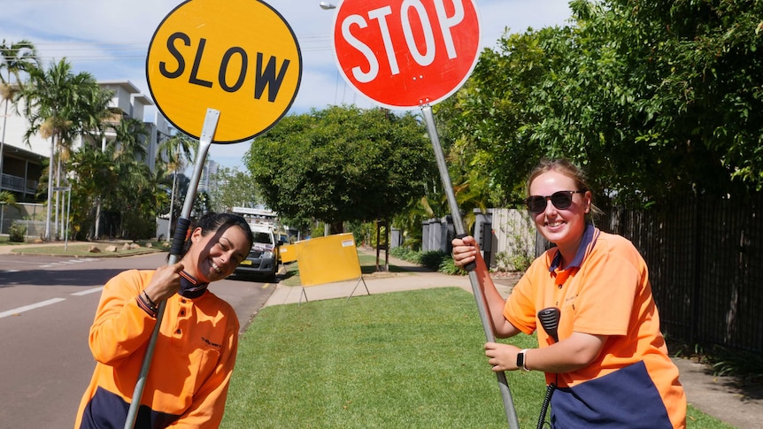 Two young women with stop and slow traffic signs smiling at camera.