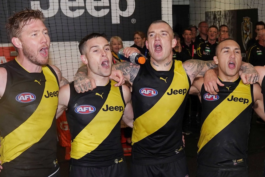 Four Richmond players, including Dustin Martin, stand arm in arm and sing the team song in the changerooms.