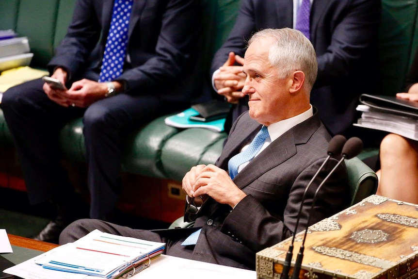 Malcolm Turnbull holds his glasses and smiles while looking at protesters in the Public Gallery.