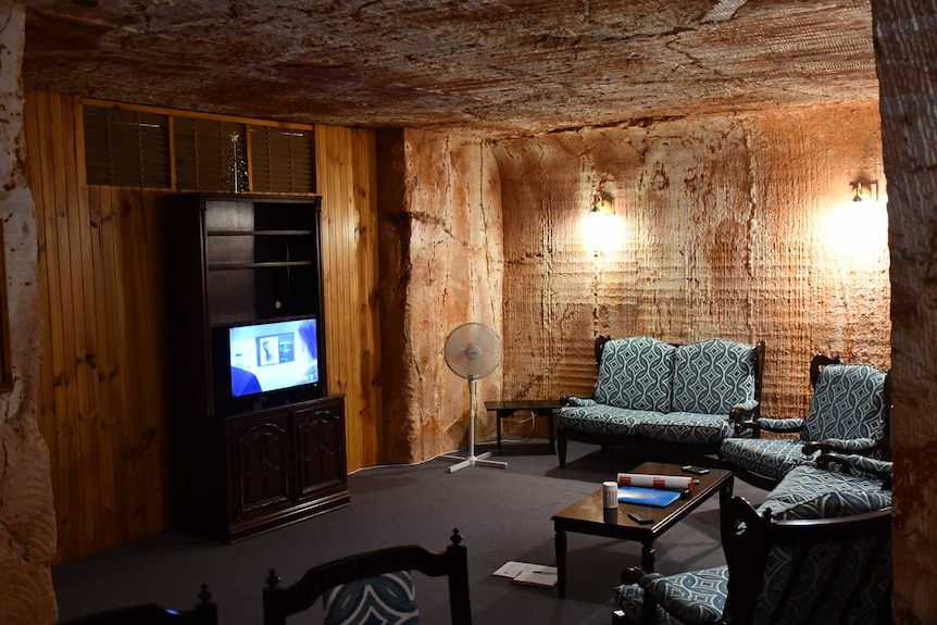 A typical living room set up with couches and a TV, except in a cave like environment, the walls are polished red sandstone