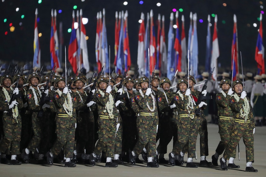 Soldiers in camouflage march holding flags and guns during a parade 