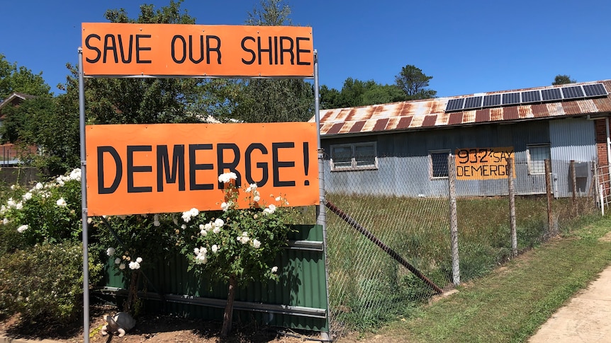 Brightly coloured signs hung on a fence that read "Save our shire" and "DEMERGE!"
